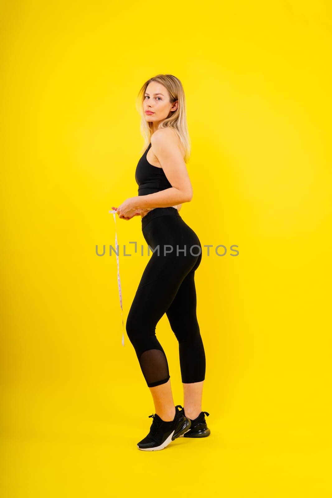 Slim body of fitness woman in a sportswear with measuring tape on waist against studio background