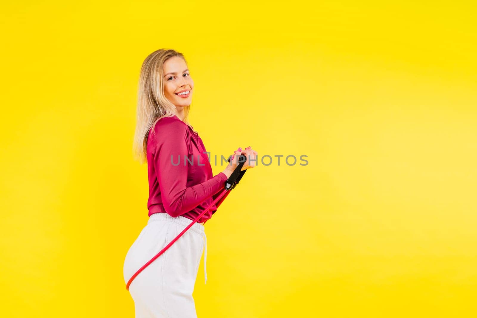 Sports woman in fashion sportswear exercising with elastic band in a studio
