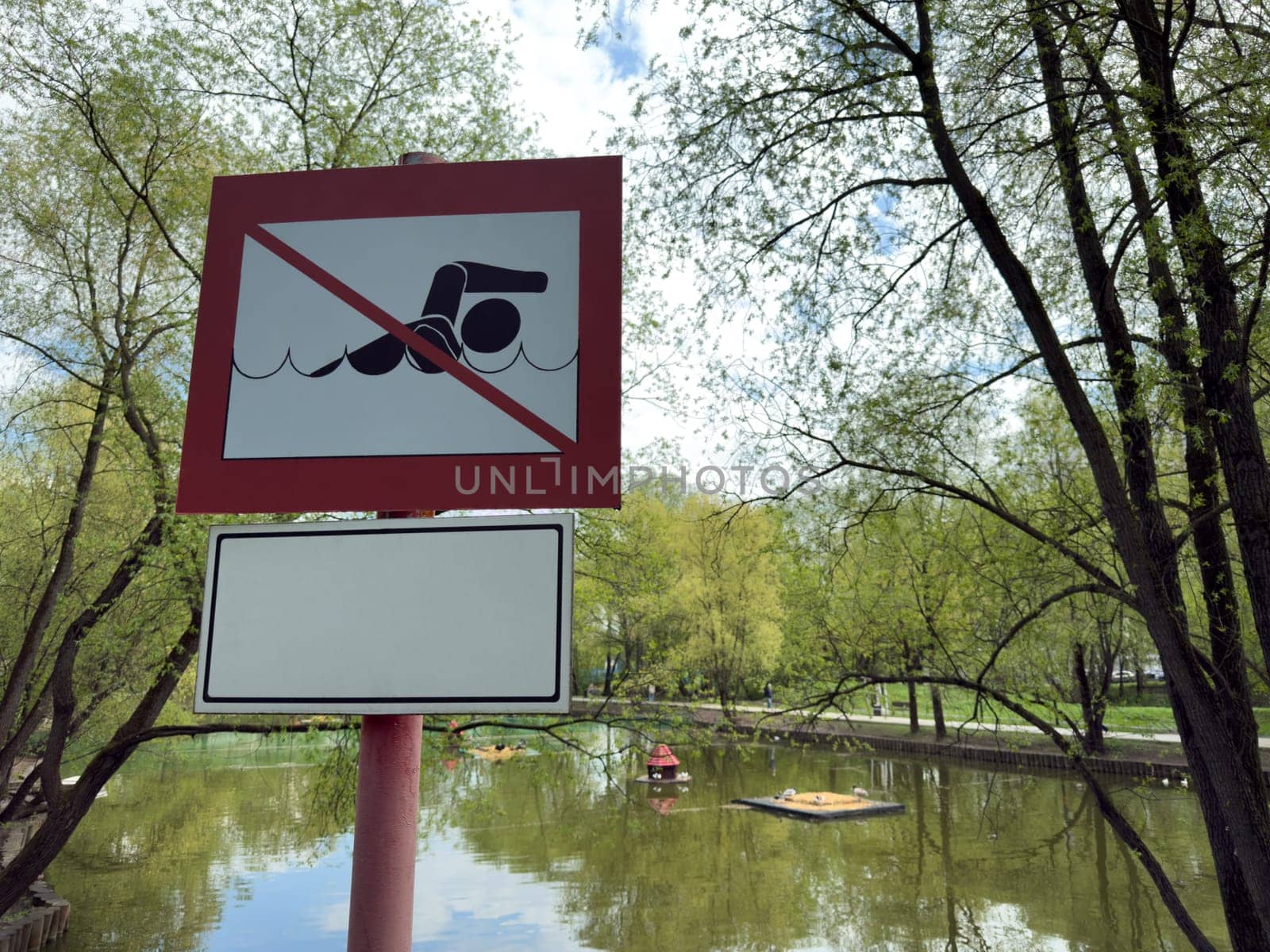 Close up of a safety sign by the pond with a clear prohibition of swimming. The warning is part of public safety measures in recreational park areas with water access