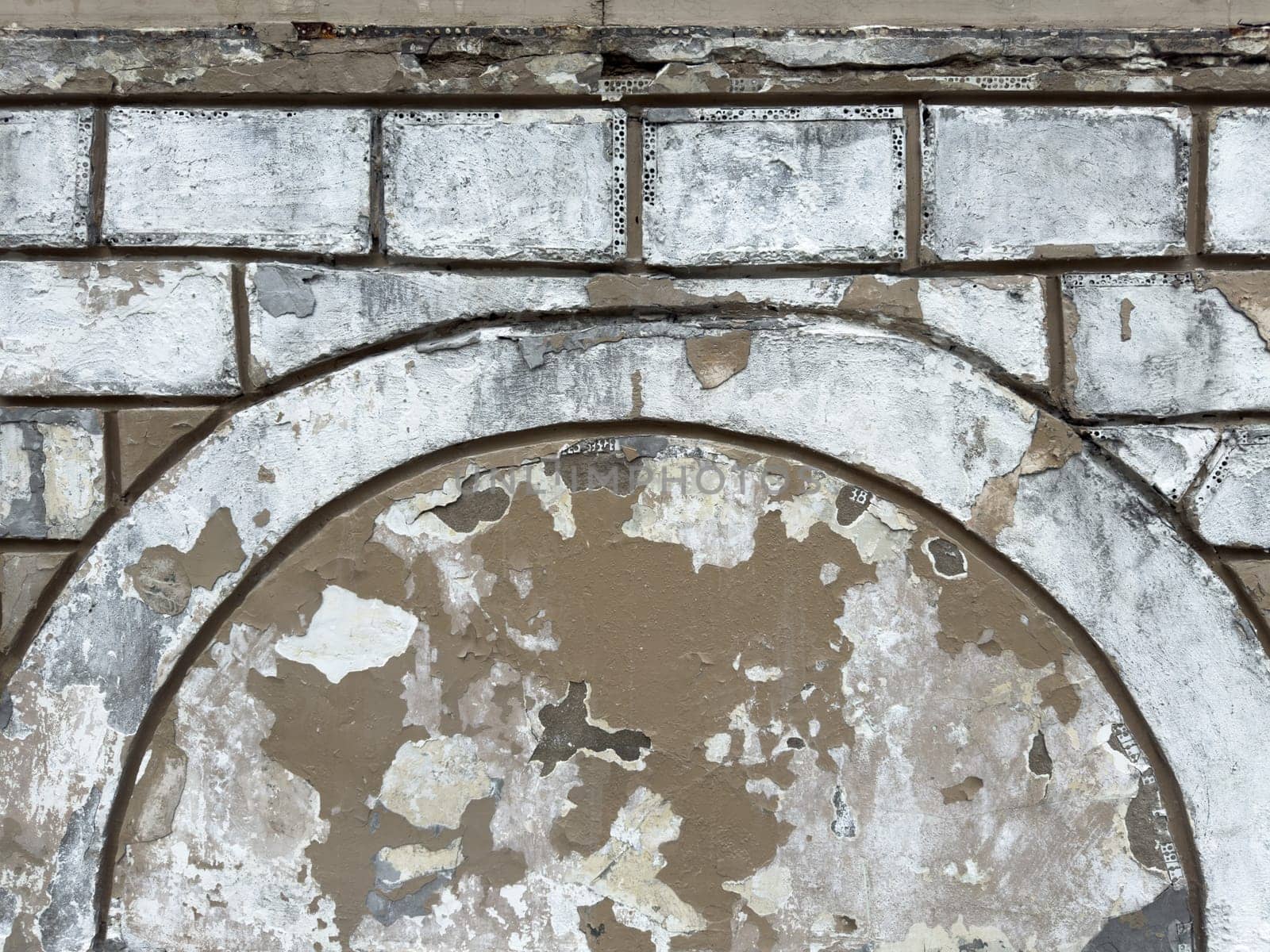 Peeling paint and rough plaster on an old brick wall form textured background with weathered surfaces and visible damage. Perfect for design or architectural texture reference