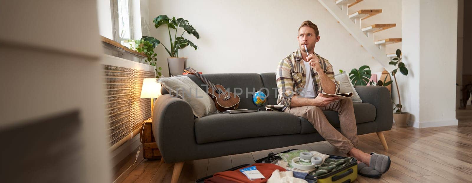 Portrait of young man packing for a trip, going on vacation, putting clothes inside suitcase, preparing for holiday.