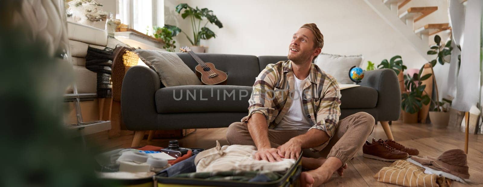 Portrait of man with suitcase, thinking what to bring on holiday, preparing for vacation, packing luggage.