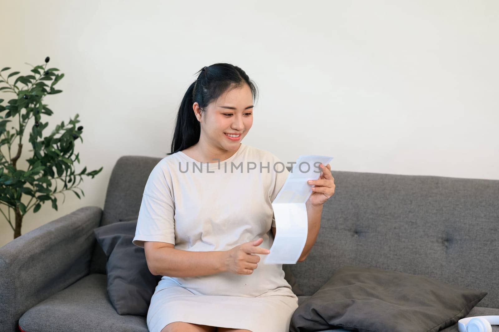 Pregnant woman admiring ultrasound pictures, gently touching her baby bump.