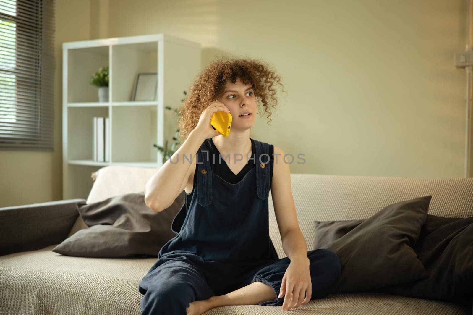 Curly haired woman having conversation on her mobile phone in a living room.