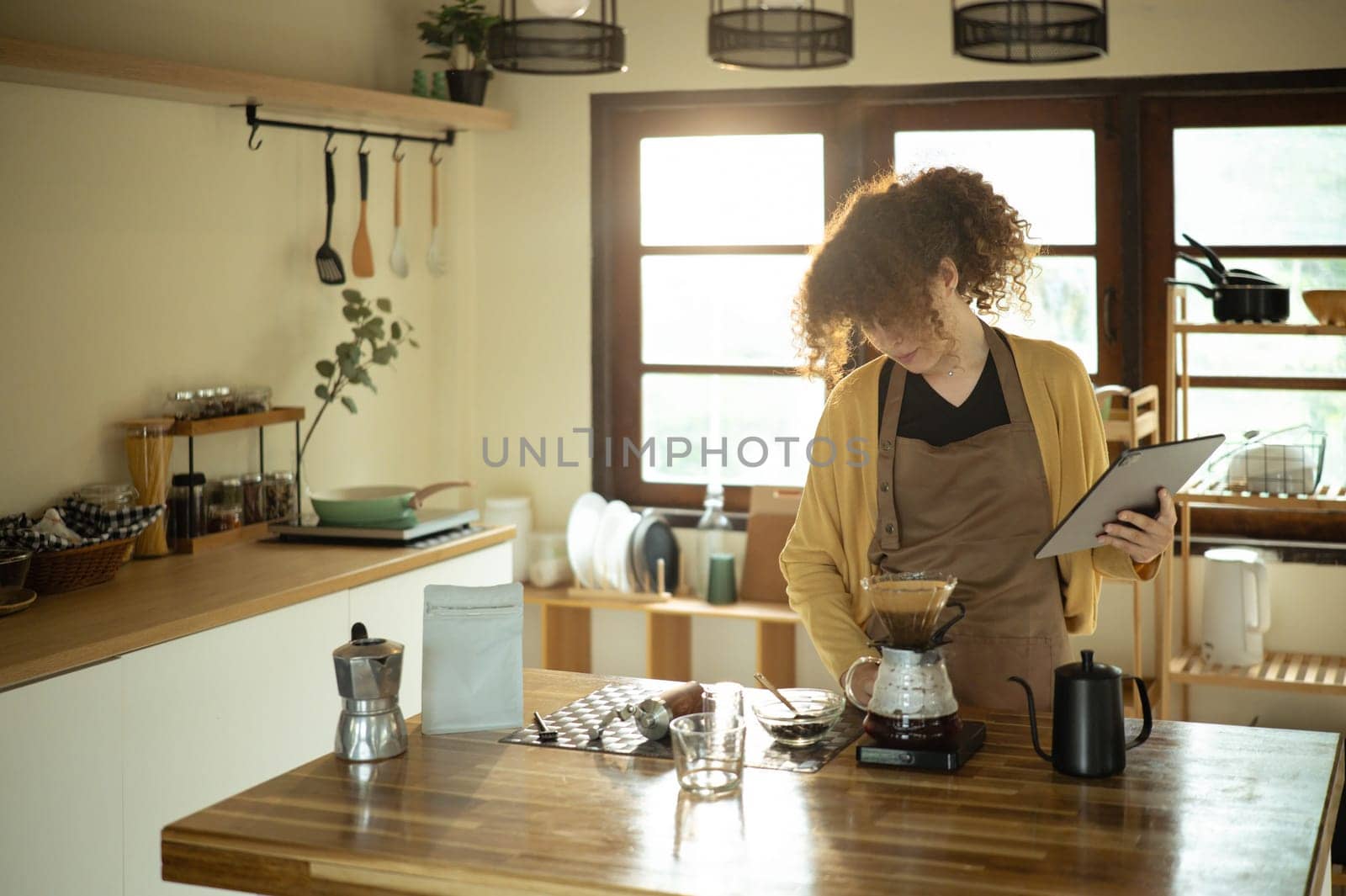 Young woman brewing pour over coffee and using digital tablet in a stylish kitchen.