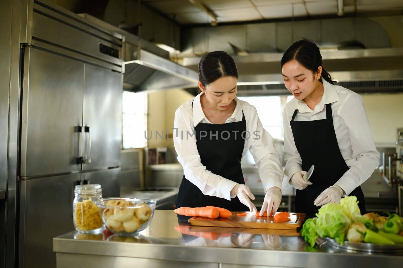 Culinary instructor guiding a student through carrot slicing during a practical cooking class.