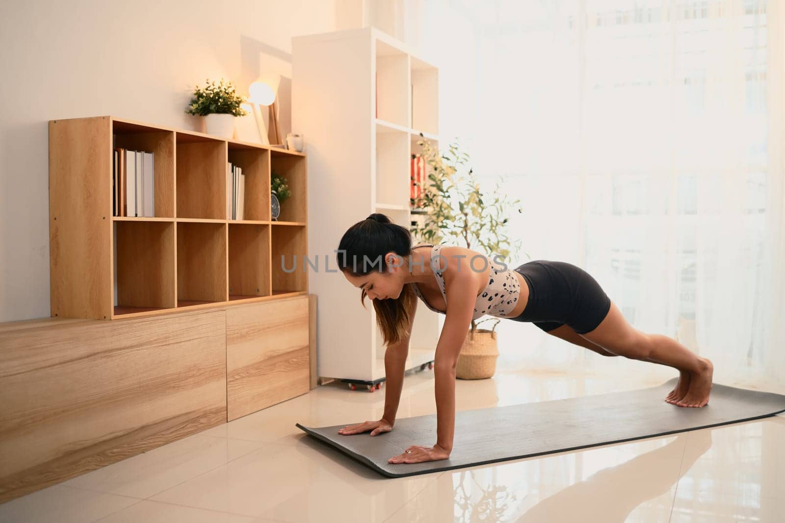 Fit young woman doing plank exercise on yoga mat at home.