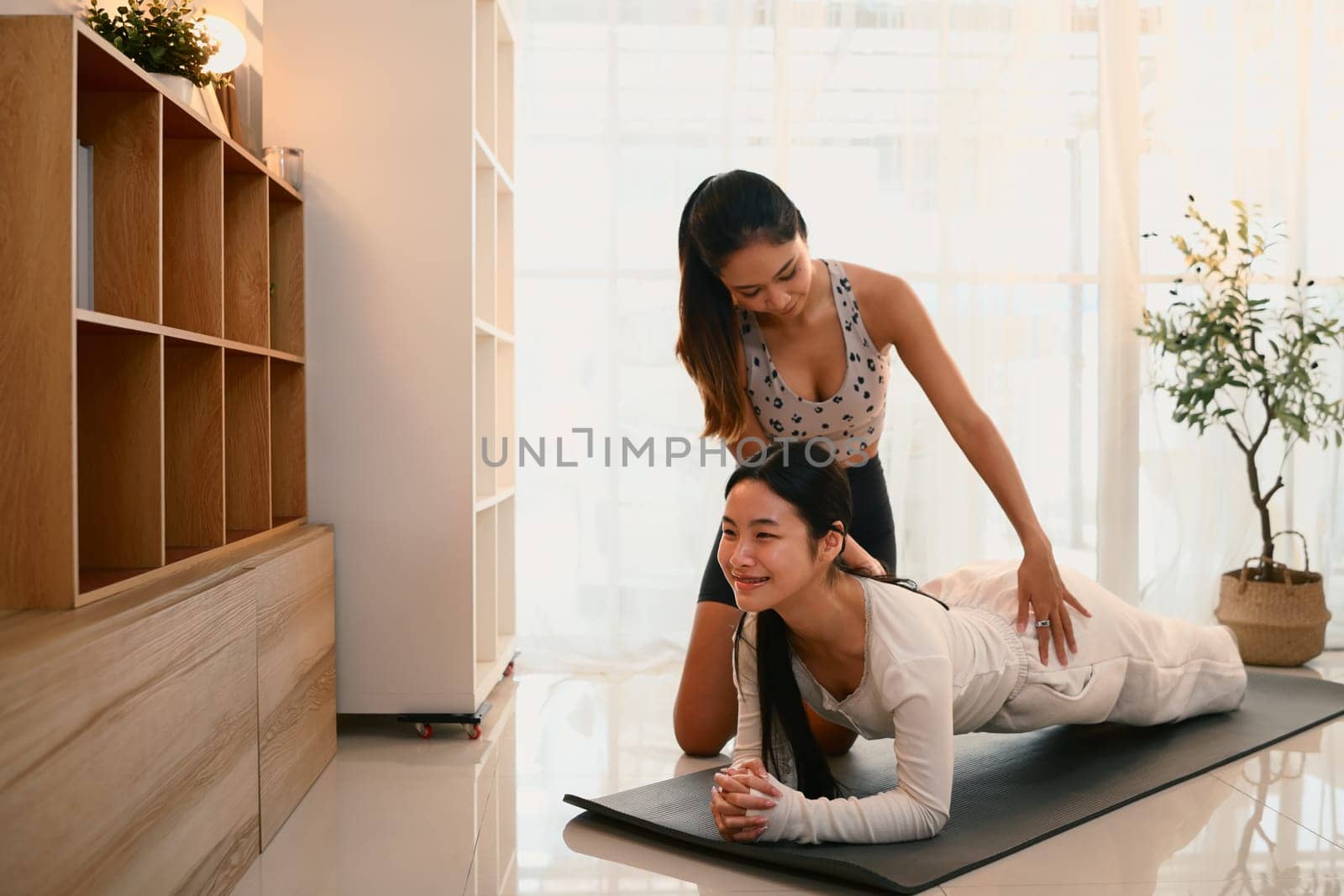 Mother guiding teenage daughter in plank exercise on mat during home workout session.