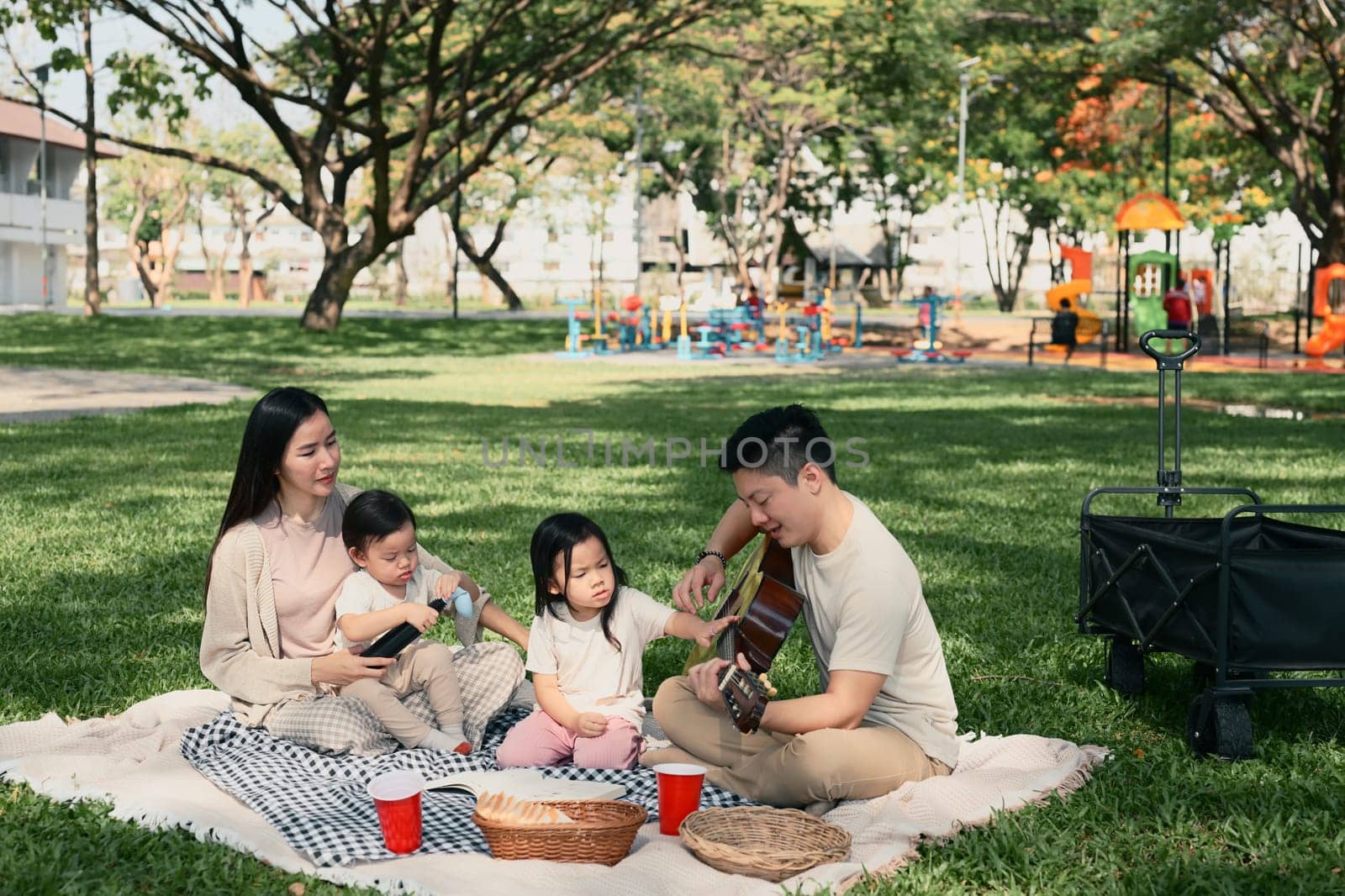 Parents and two children sharing a joyful outdoor meal during a weekend picnic in a green park.