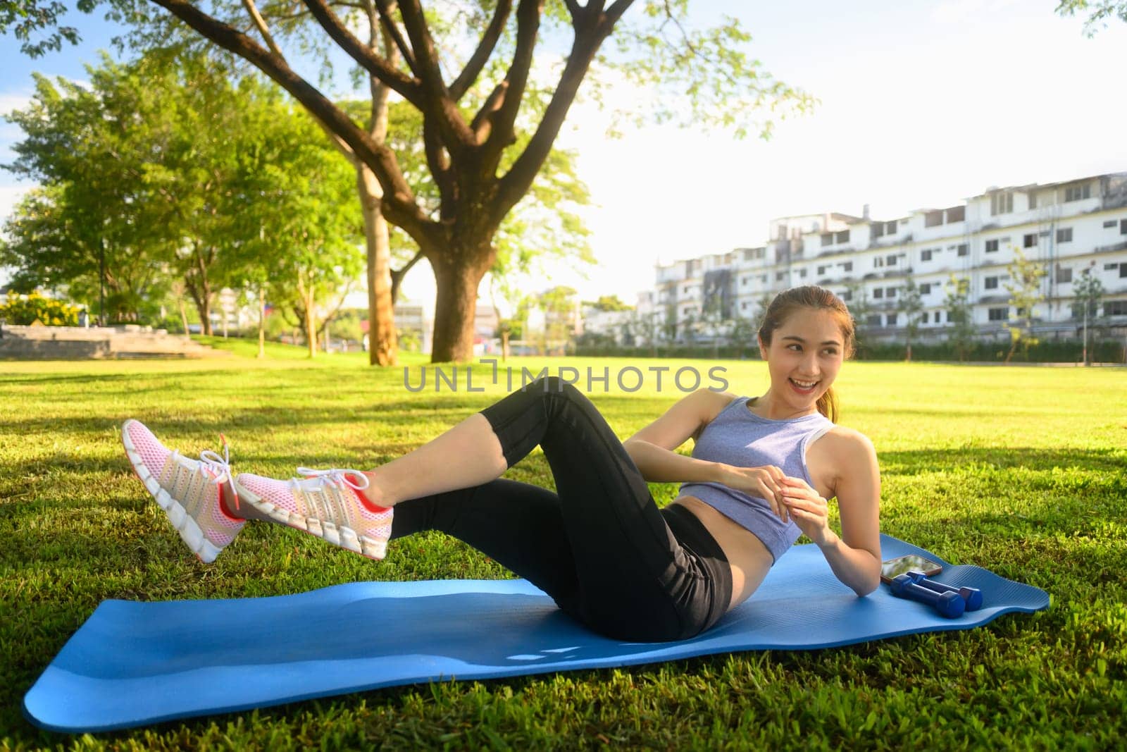 Young woman doing abdominal exercises on a yoga mat in the park.