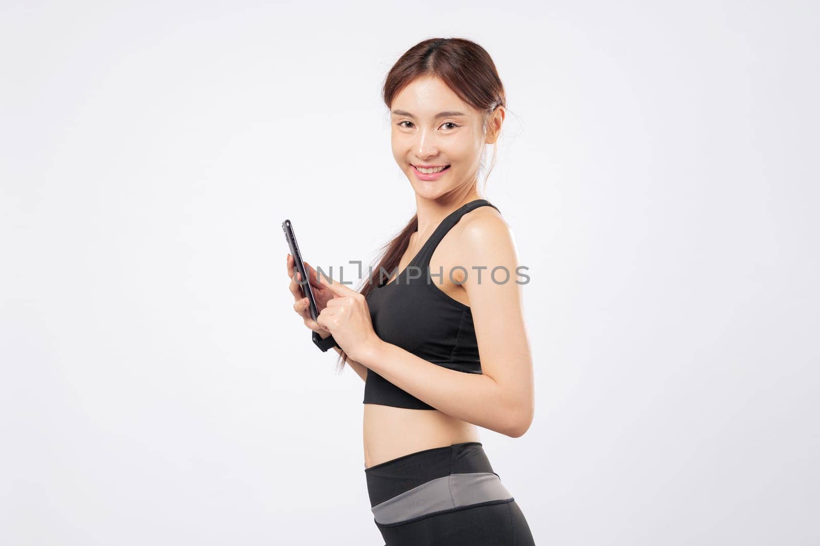 Phone ready and using her phone to check fitness progress, this athletic woman in black activewear blends gym strength and smartphone ease in one inspiring portrait. isolated studio white background