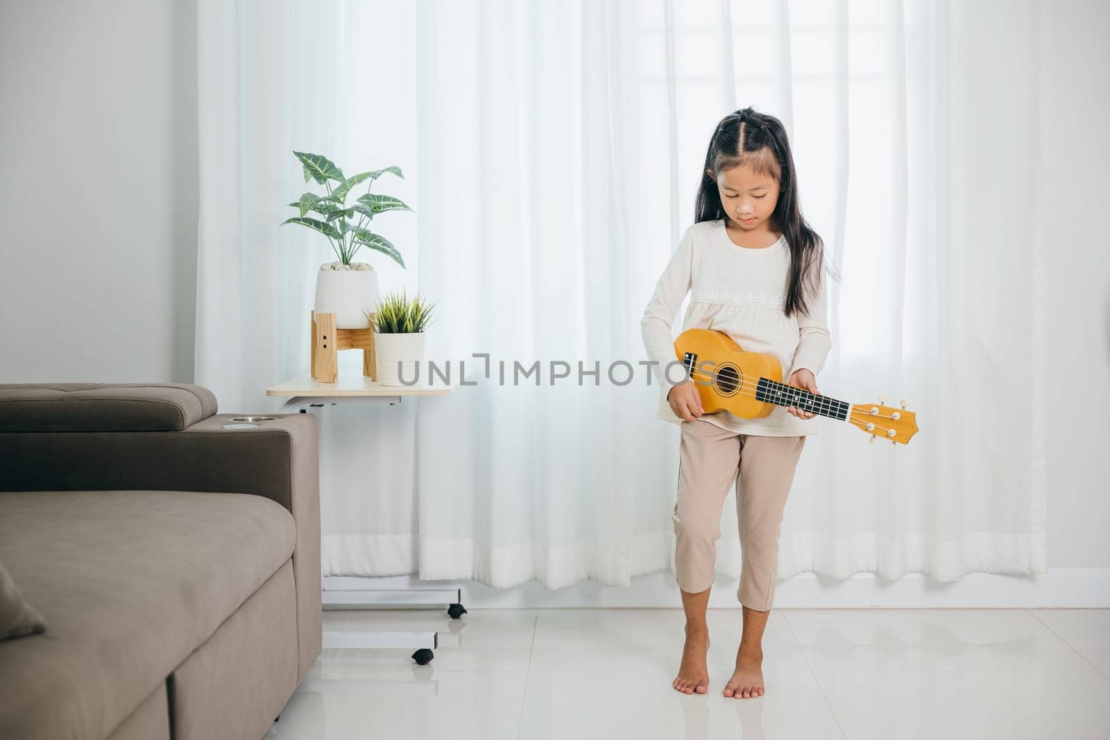 An Asian girl stands in a stylish living room, ukulele in hand, her expression full of joy. The scene reflects her passion for music and adds a charming artistic touch to the modern setting.