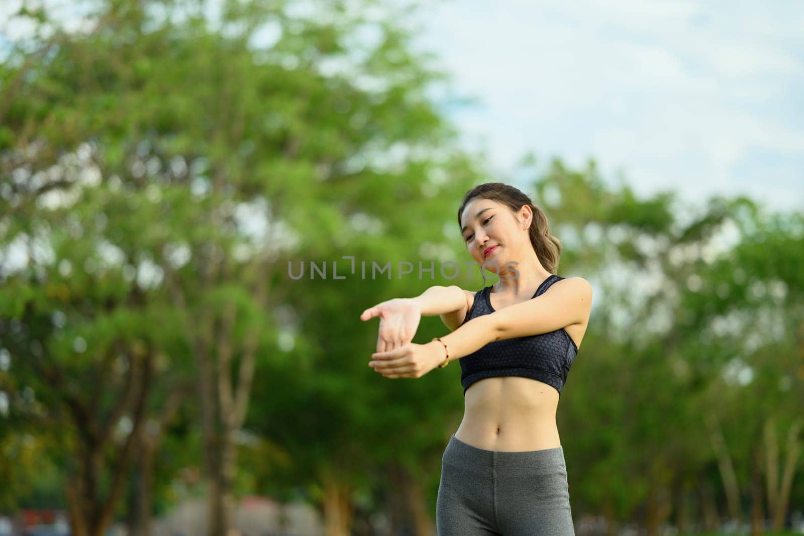 Beautiful woman in sportswear stretching her body in a lush green park.