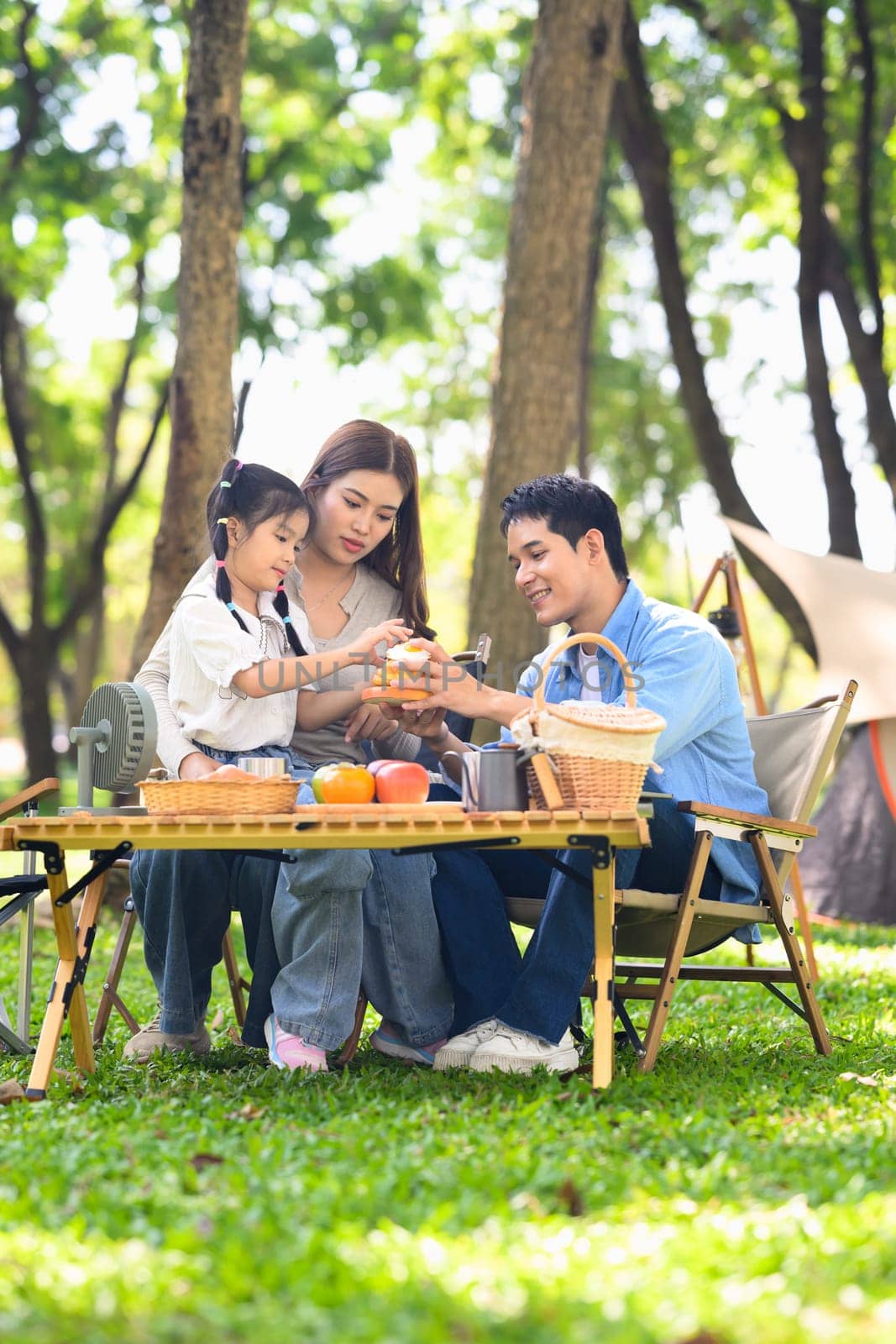 Happy family enjoying breakfast at a table while camping in a forest park.