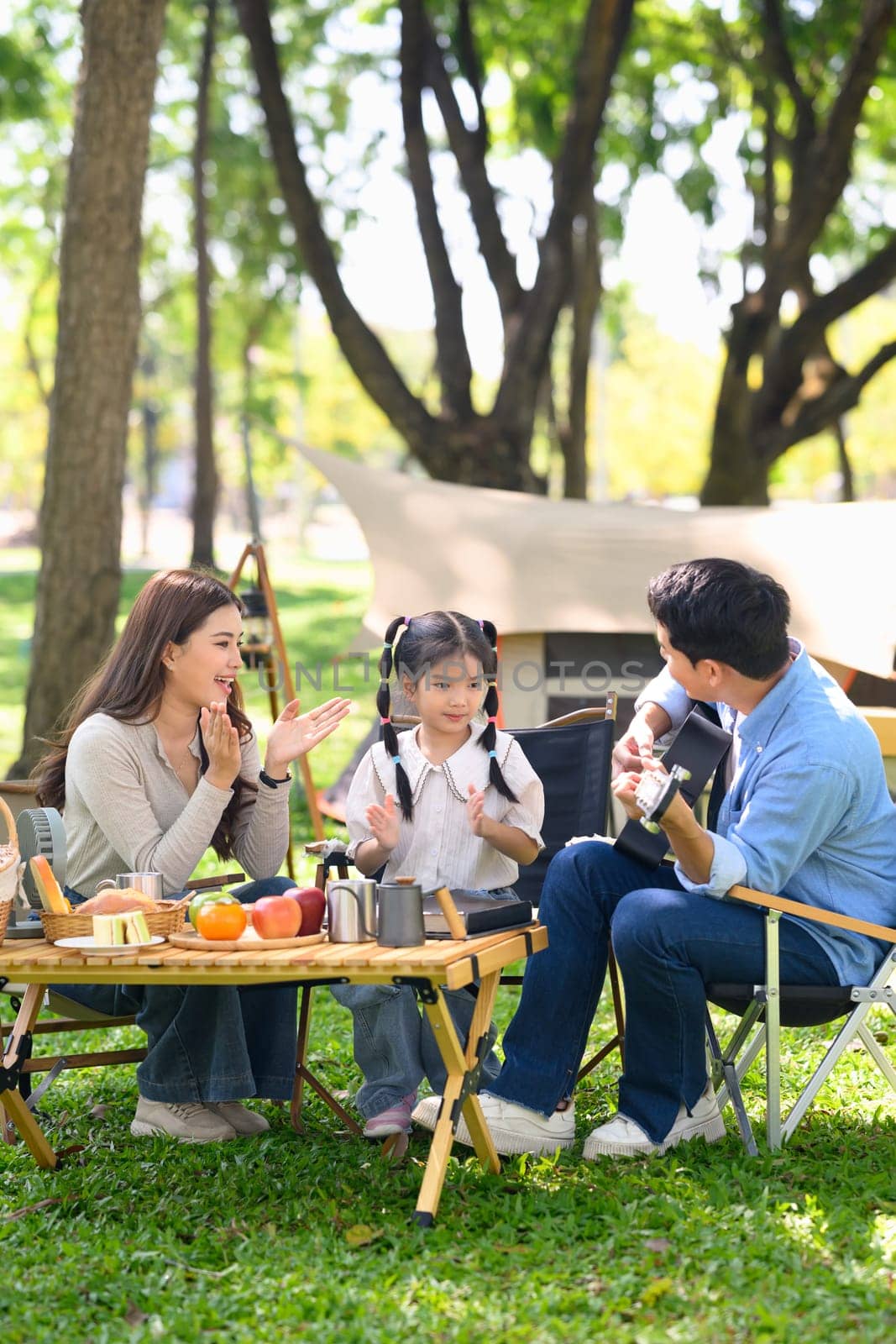 Parents and daughter camping in a forest park surrounded by nature and fresh food.