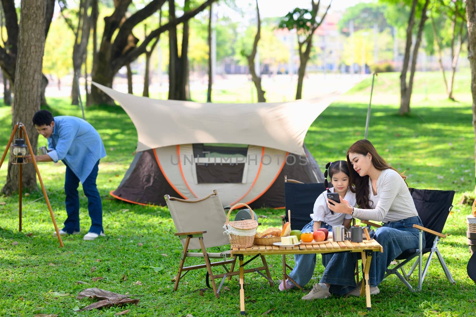 Happy mother and child seated near a tent enjoying time while camping under the trees.