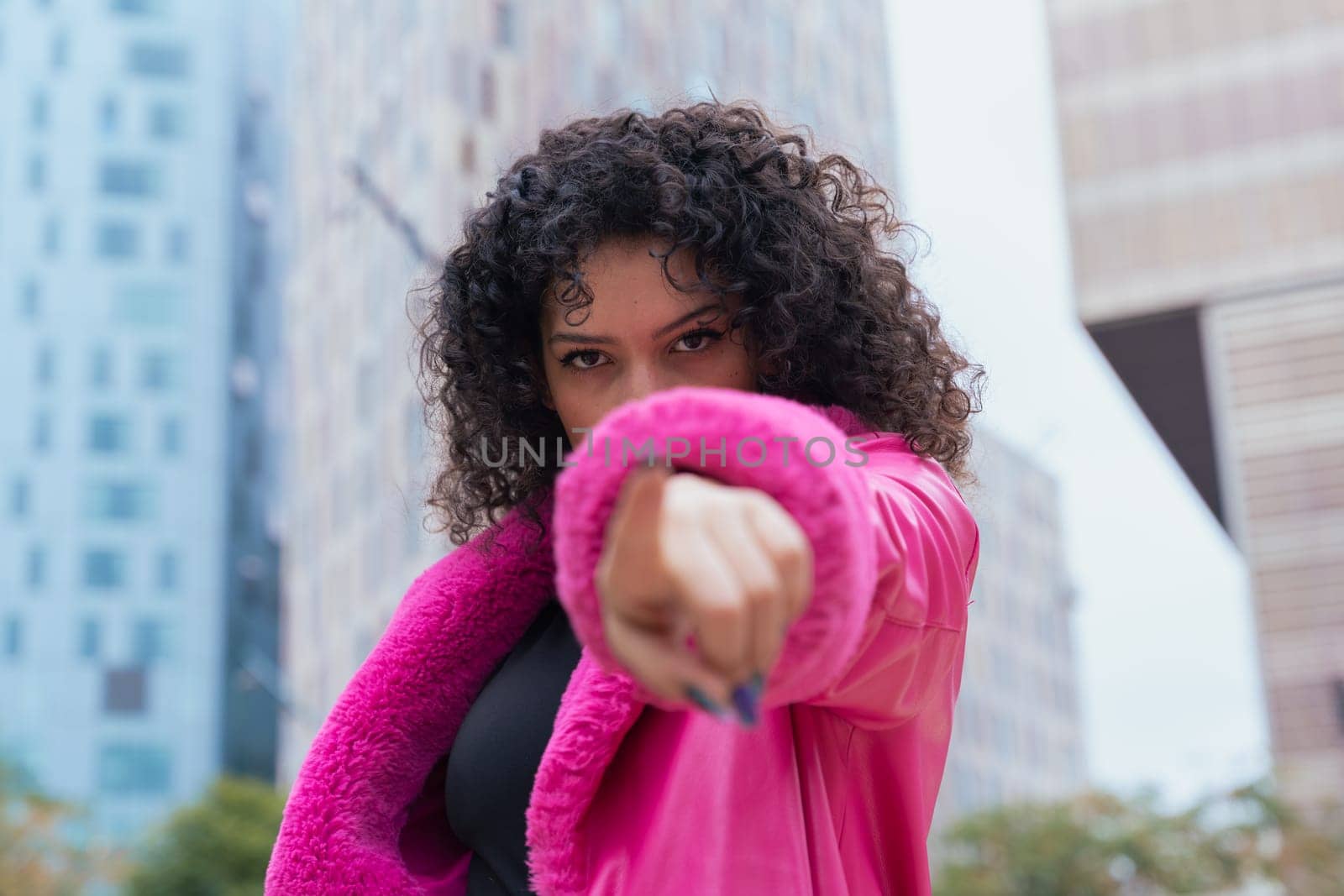 Graceful dancer with curly hair wearing a pink coat, expressing movement and energy in an urban environment. Modern fashion, contemporary dance, and artistic performance against a city backdrop.