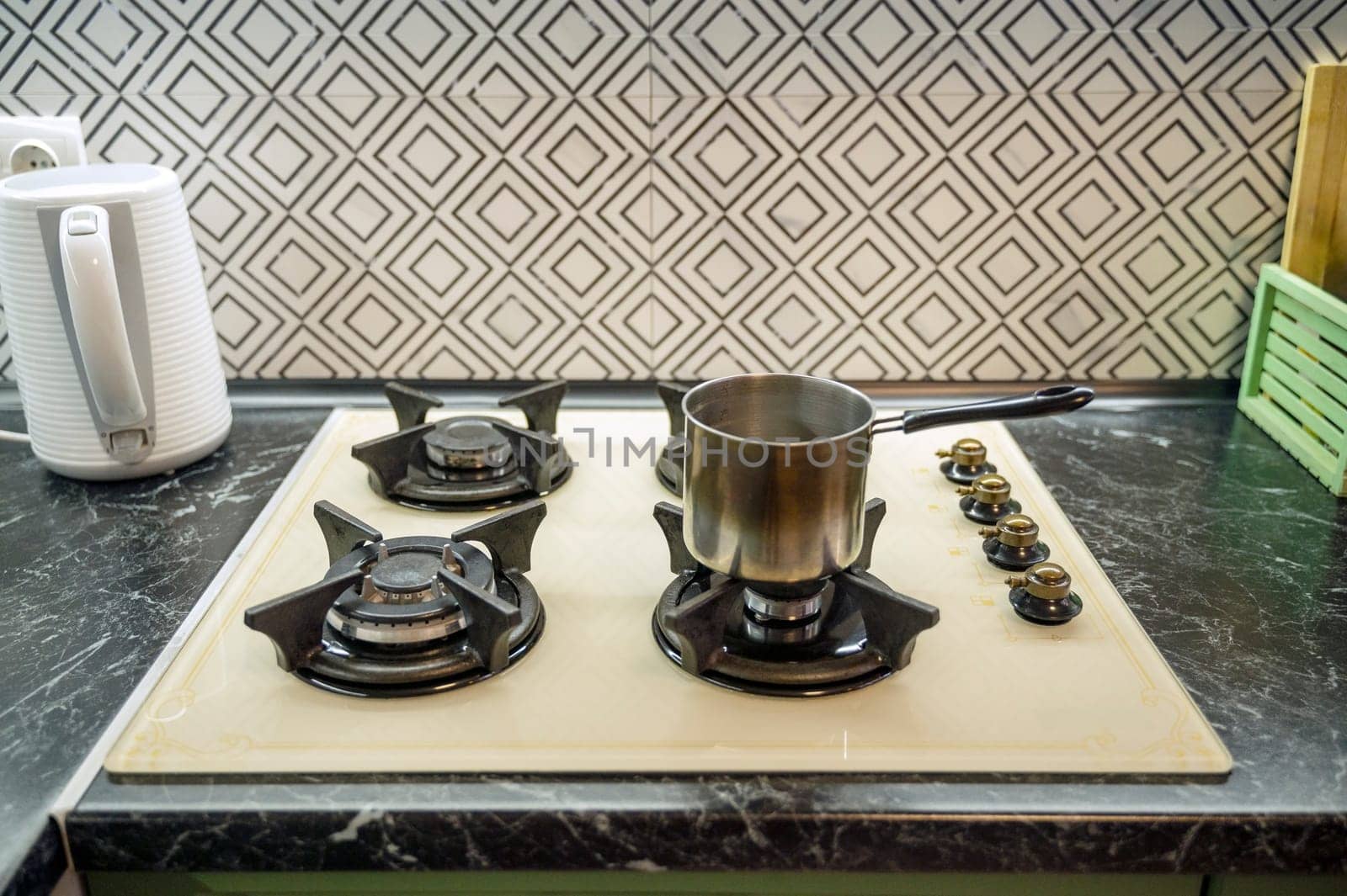 Close-up of a saucepan on a gas stove in a kitchen interior. Light beige gas panel, white electric kettle nearby.