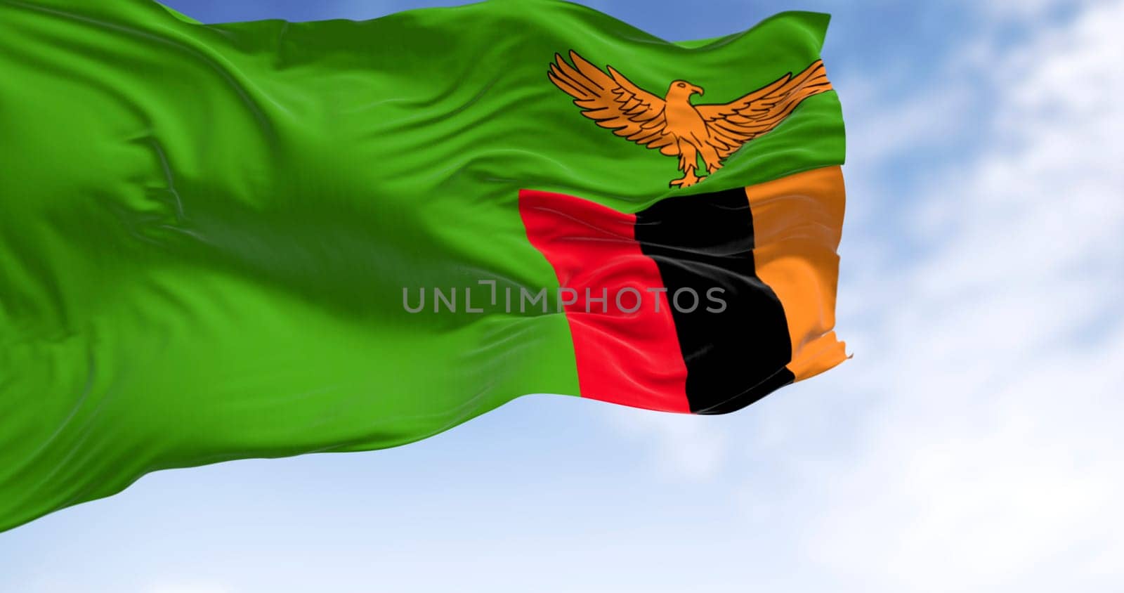 Zambia national flag waving in the wind. Green with an orange eagle in flight over a block of three vertical stripes in red, black, and orange. 3d illustration render. Selective focus