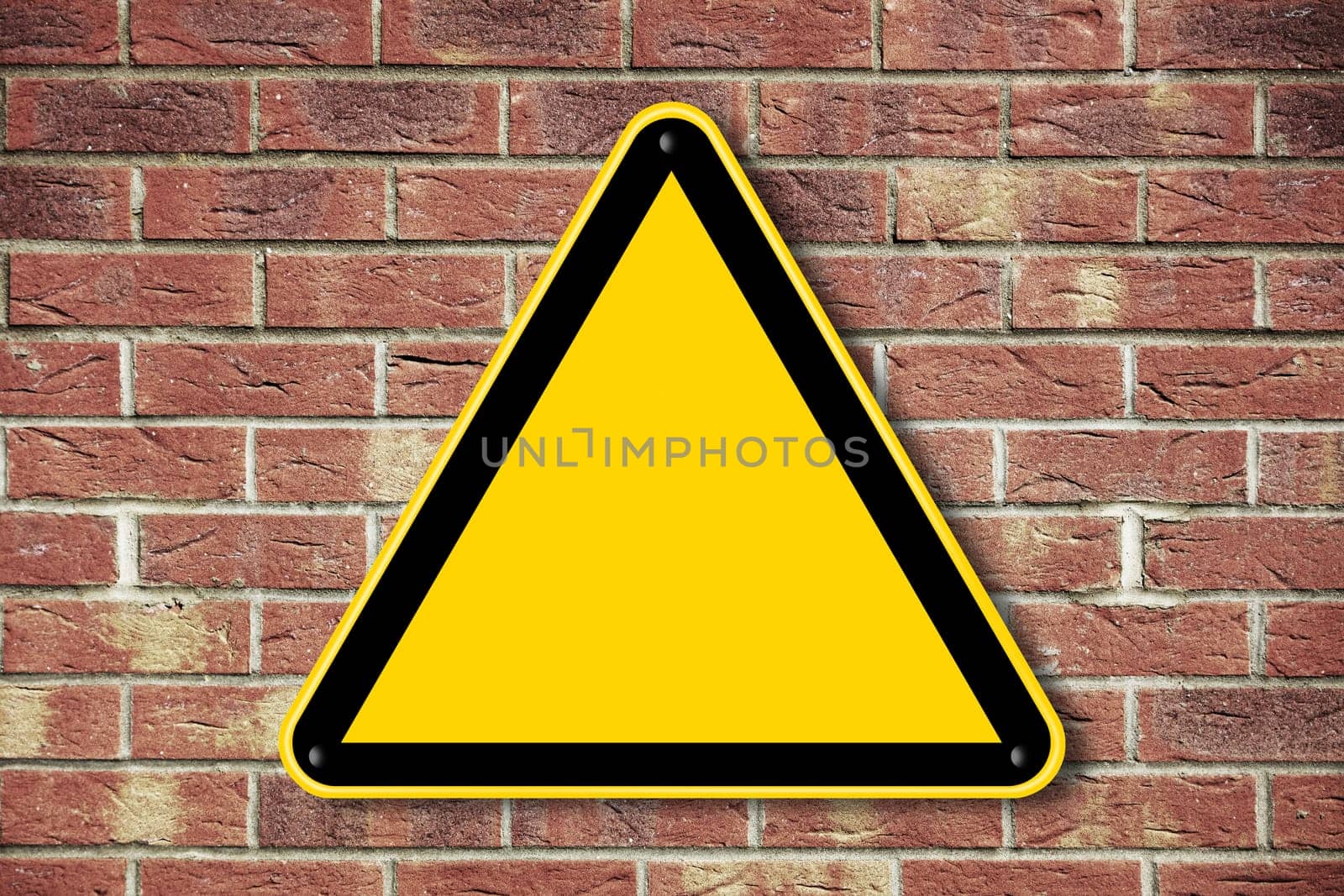 A blank yellow caution triangle sign on a brick wall with copy space