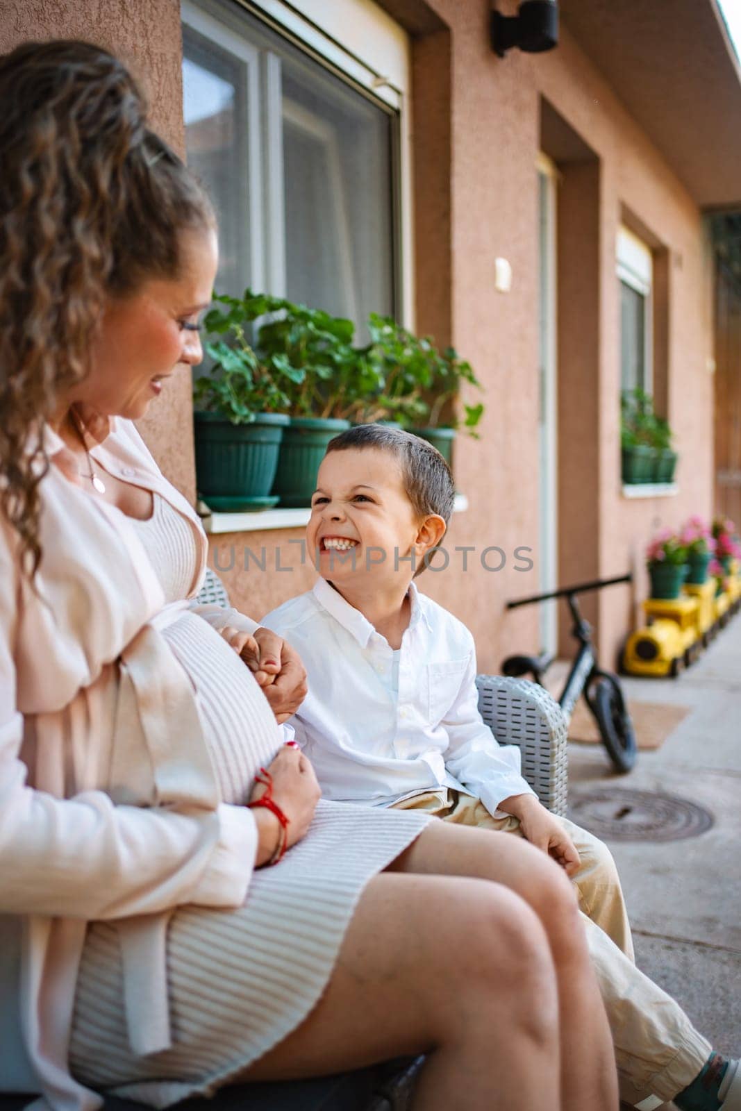 A young boy smiles lovingly at his mother's pregnant belly.