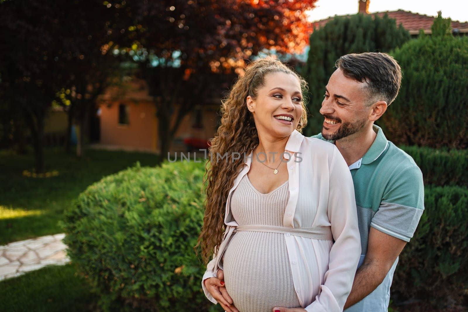 A couple embraces in a lush garden anticipating their baby.