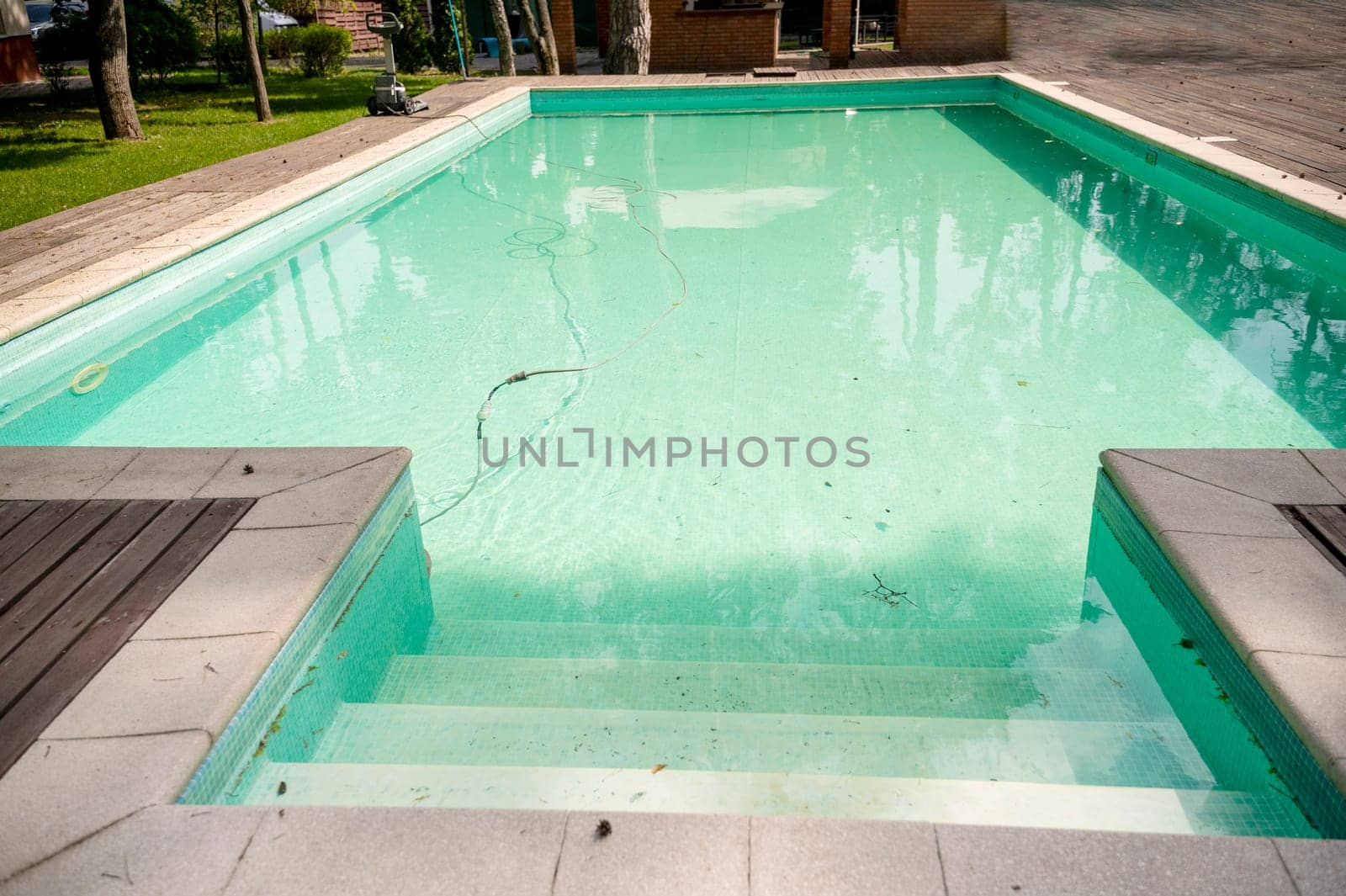 A swimming pool with wooden decking in the garden of a luxury hotel, and water purification equipment. The pool has a machine for cleaning the pool.