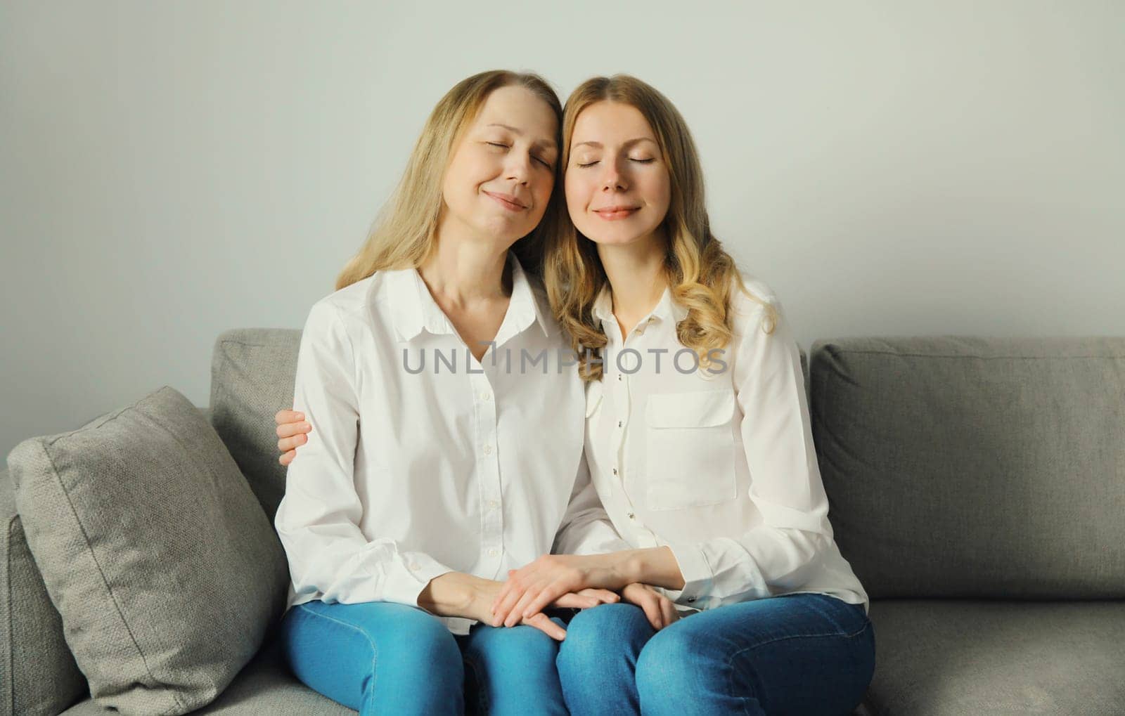 Portrait of happy two women, smiling mature mother and adult daughter together hugging sitting on couch in living room at home, warm family feelings