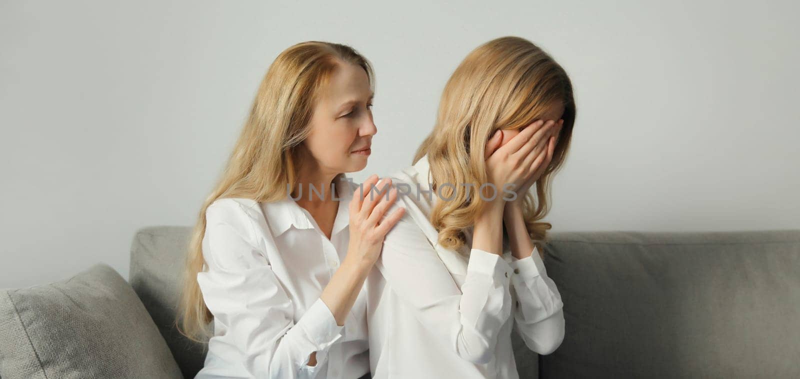 Upset offended caucasian two women, mature mother or sister and adult daughter crying together sitting on couch at home