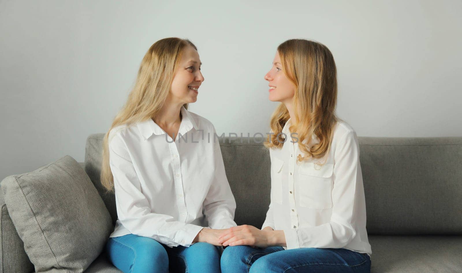 Happy smiling caucasian two women talking, mature mother or sister and adult daughter looking at each other together sitting on couch in living room at home