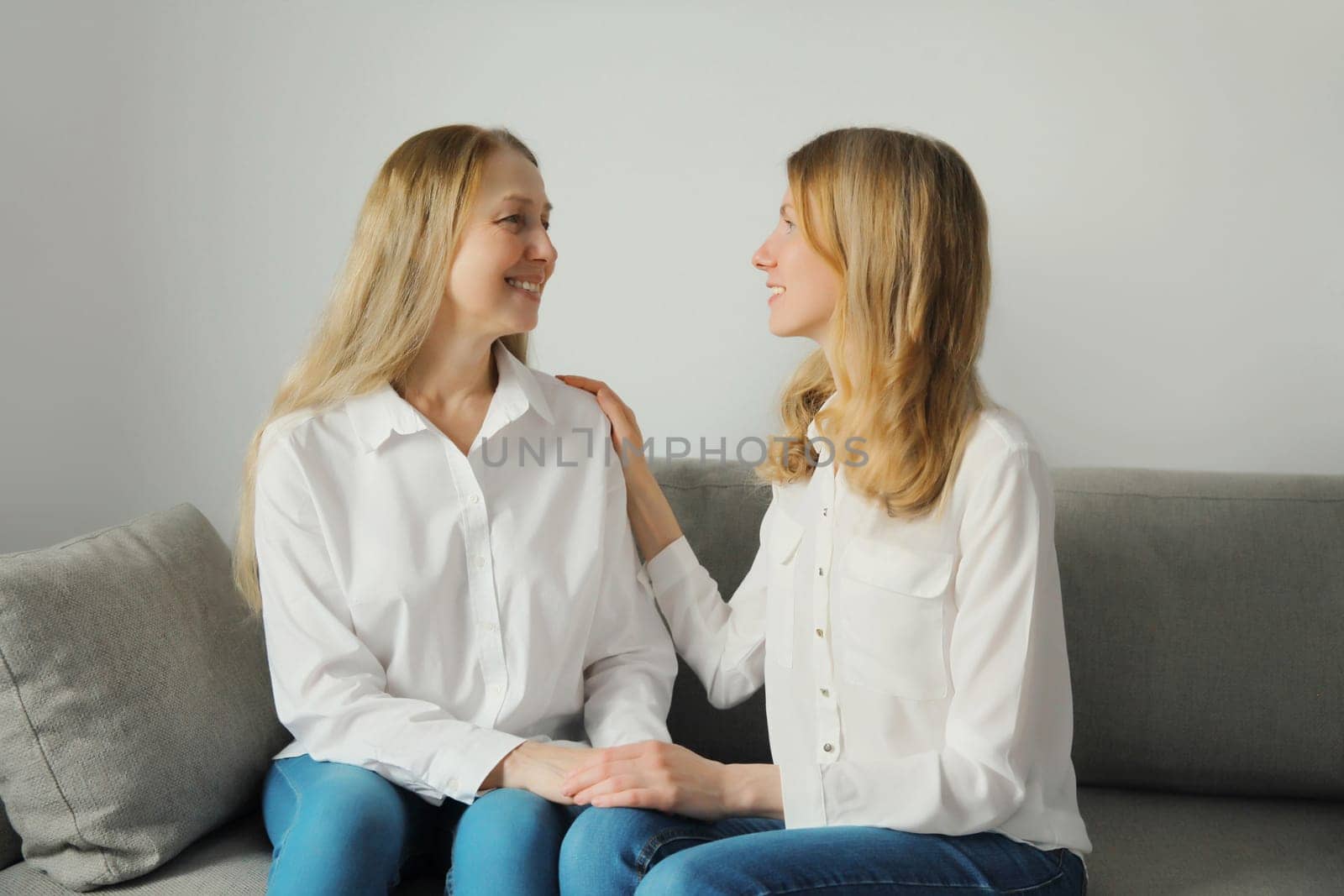 Happy smiling caucasian two women talking, mature mother or sister and adult daughter looking at each other together sitting on couch in living room at home