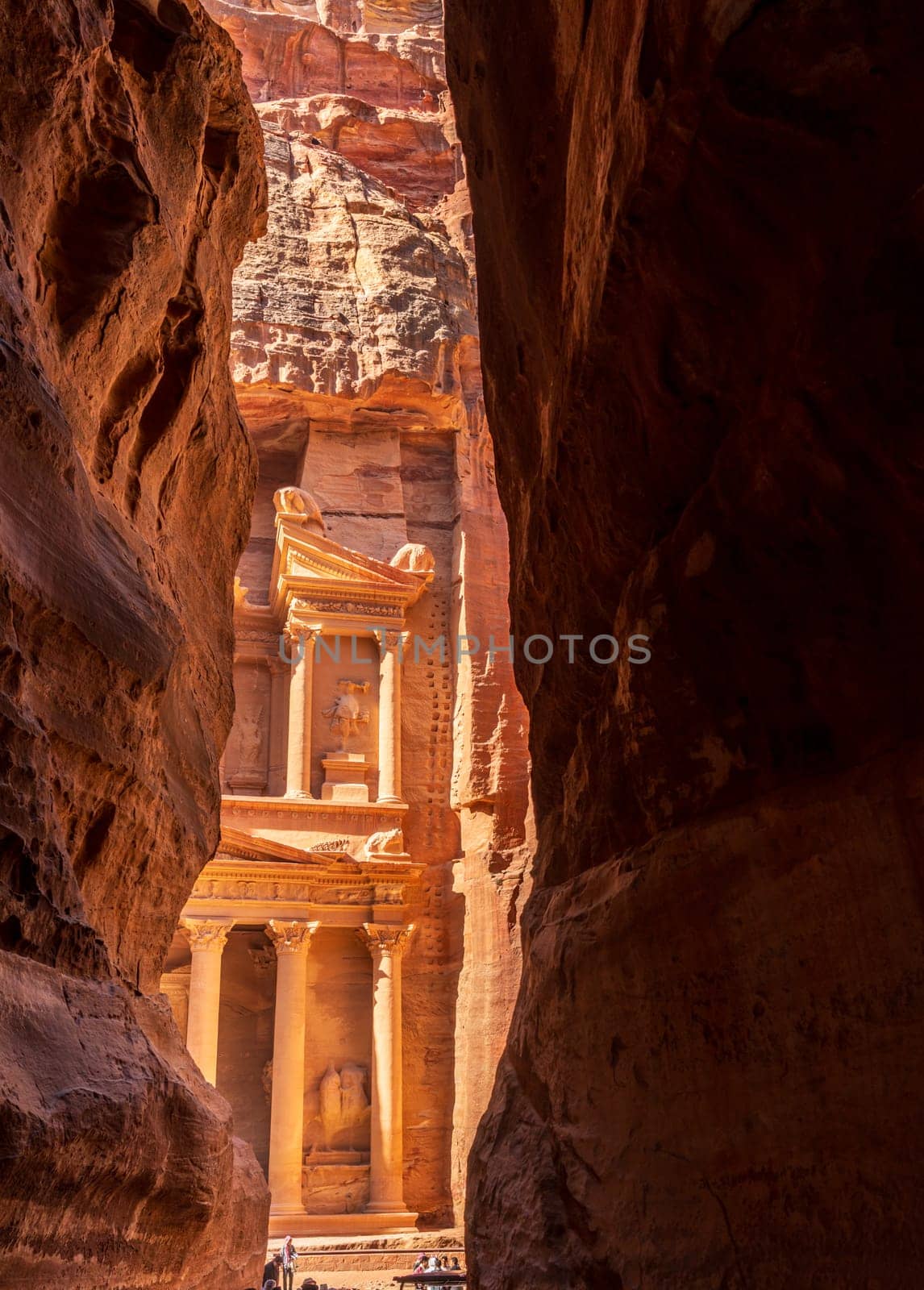 The carved facade of the Treasury building or Al-Khazneh in the ancient city of Petra in Jordan seen through narrow Siq gorge