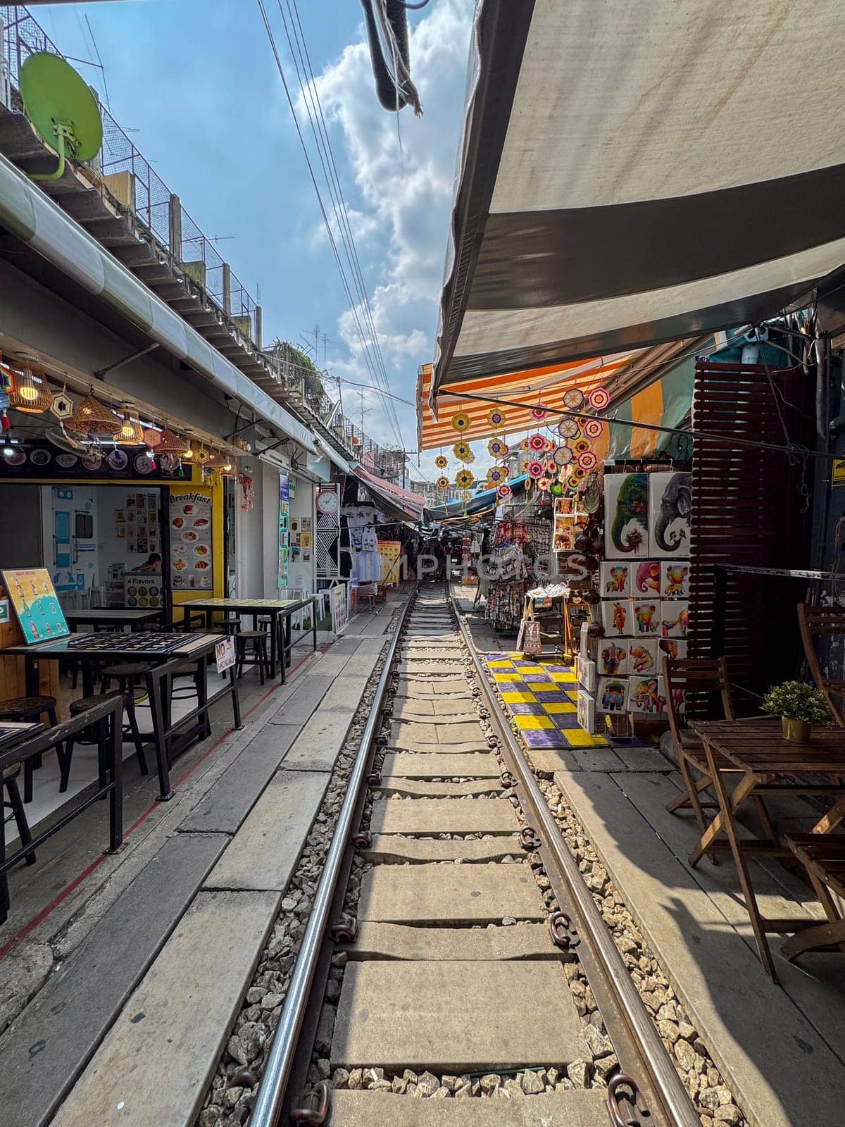 Bangkok, Thailand - November 12, 2024: Tourists pass through Thai railway market, where train moves through busy street market with vendors selling fruits, vegetables and local Thai food.
