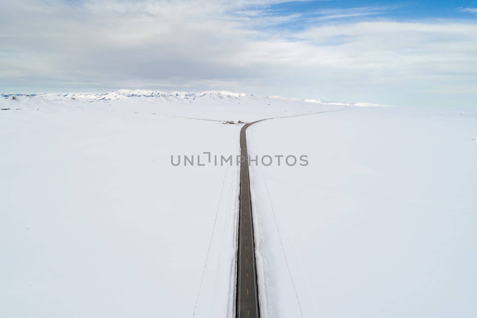 A long road in the snow with no cars on it. The sky is cloudy and the road is empty