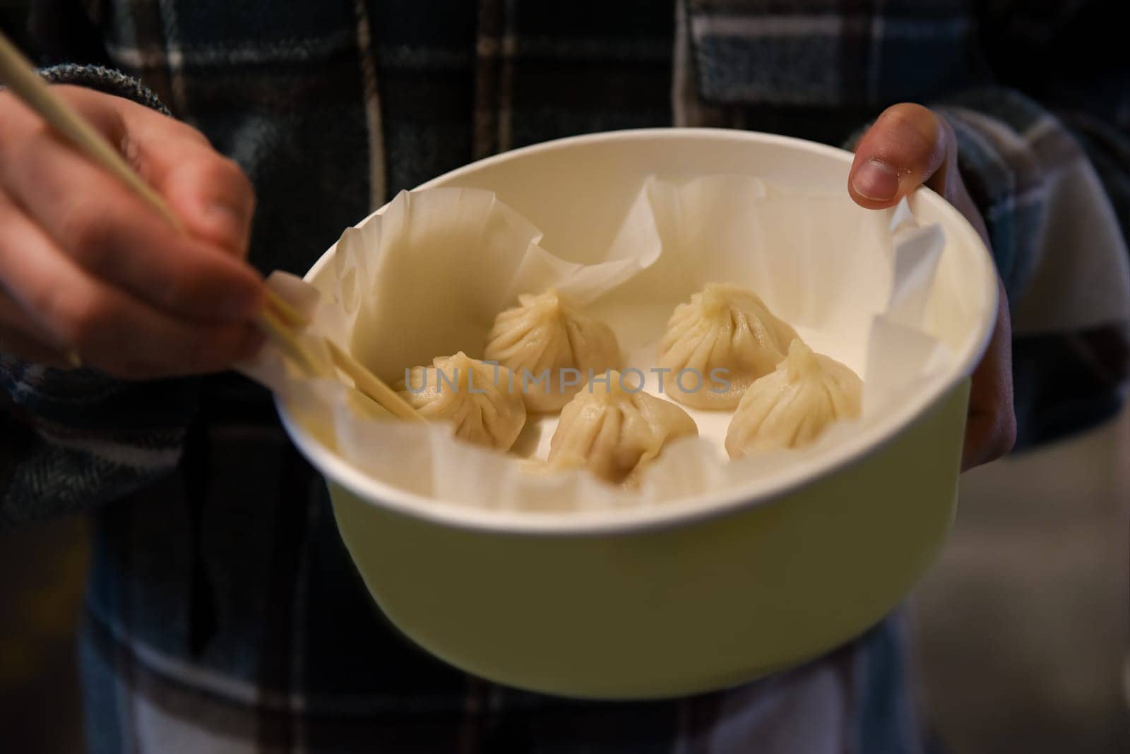 Close-up of Chinese crab and pork dumplings in a bowl held by a tourist on Yuyuan Old Street in Shanghai, with chopsticks ready to pick one