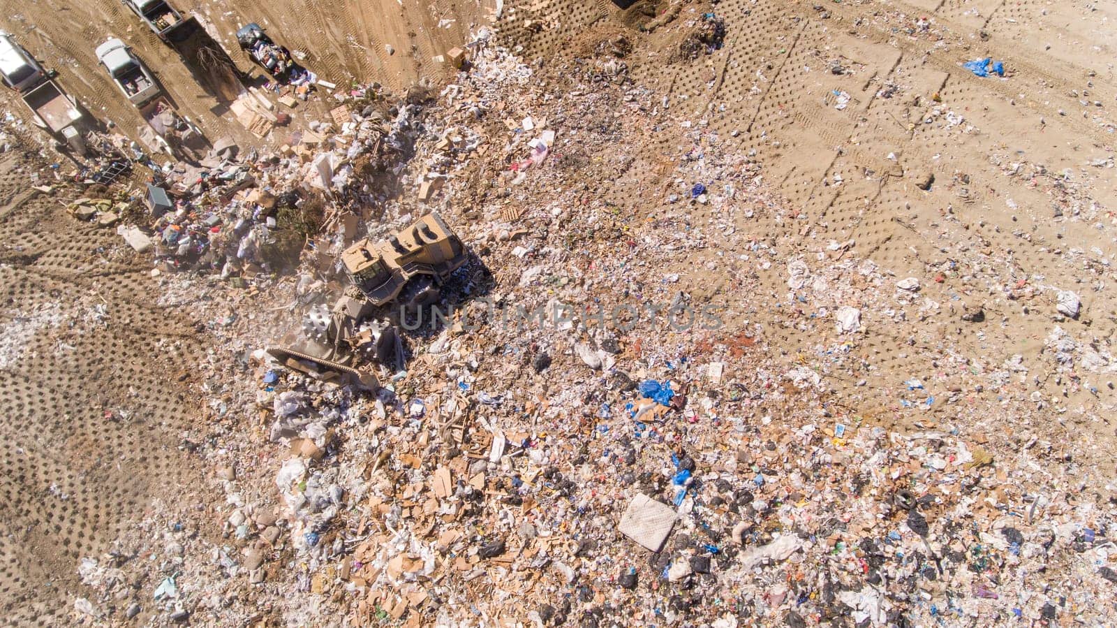 A large dumpster is seen in the middle of a pile of trash. The trash is scattered all over the ground, and the dumpster is surrounded by a lot of debris. The scene is chaotic and messy
