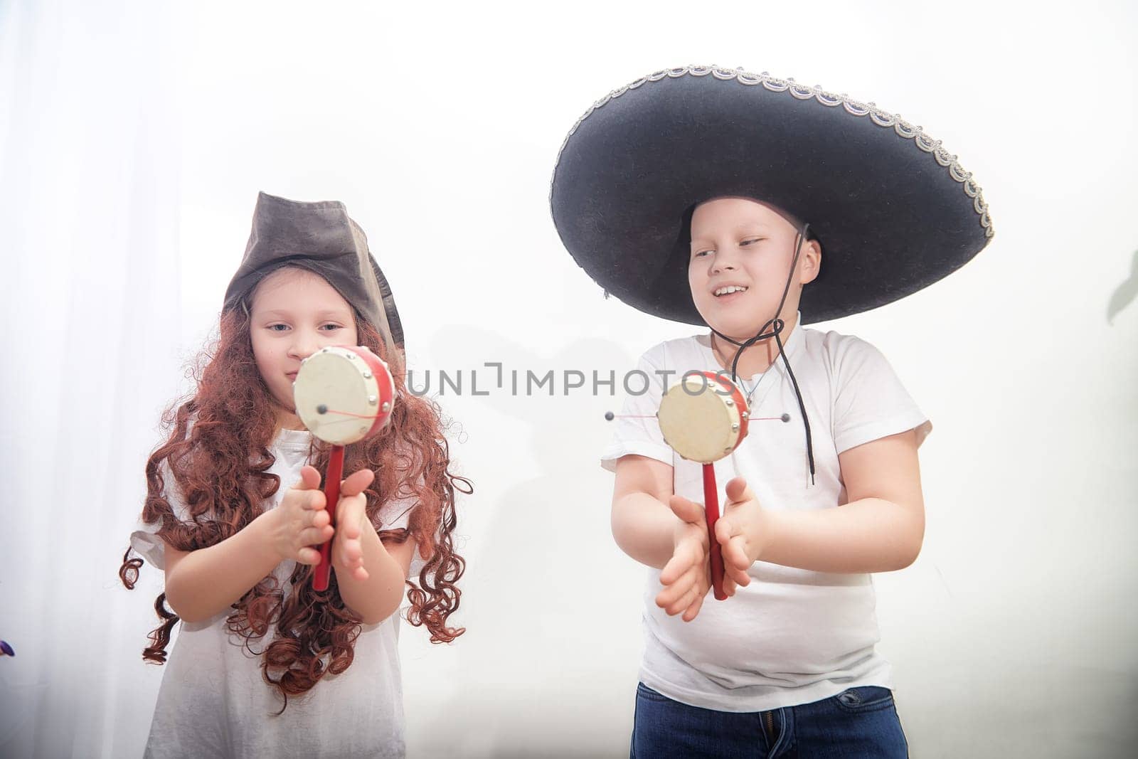 Two children play tambourines, wearing colorful hats while celebrating a joyful occasion together, surrounded by festive decor.