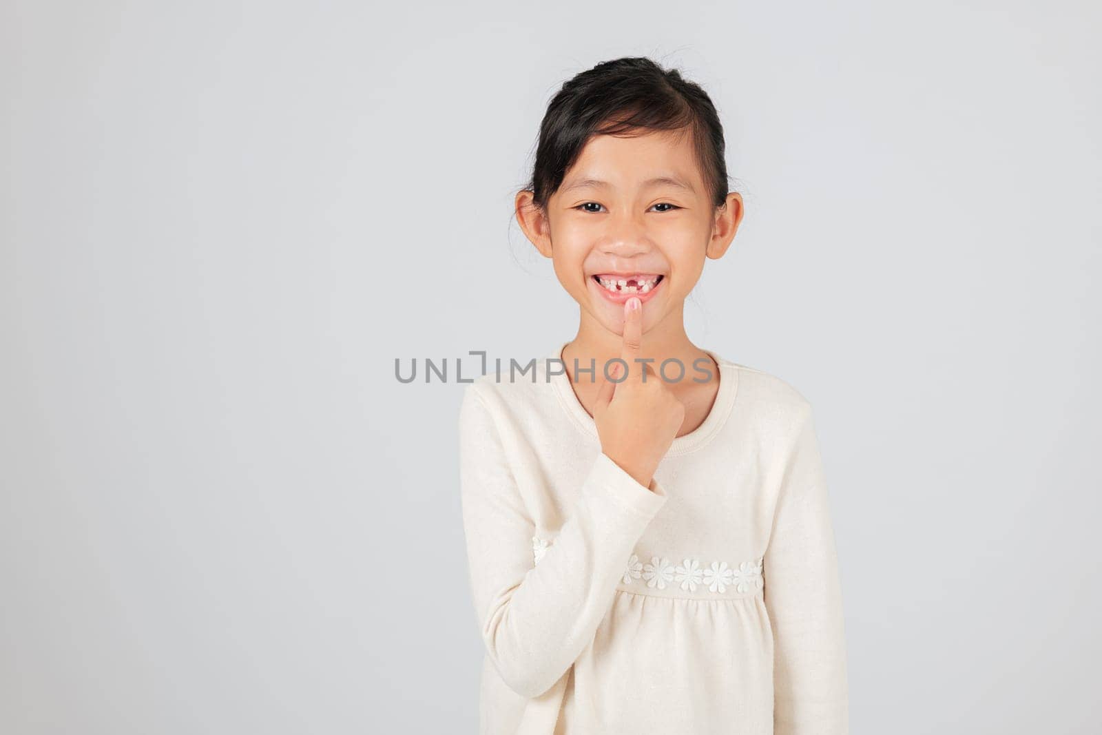 Schoolgirl pointing at her tooth gap, smiling brightly. The dentist educates on the natural process of tooth loss and how the new tooth gap affects dental development. isolated white background