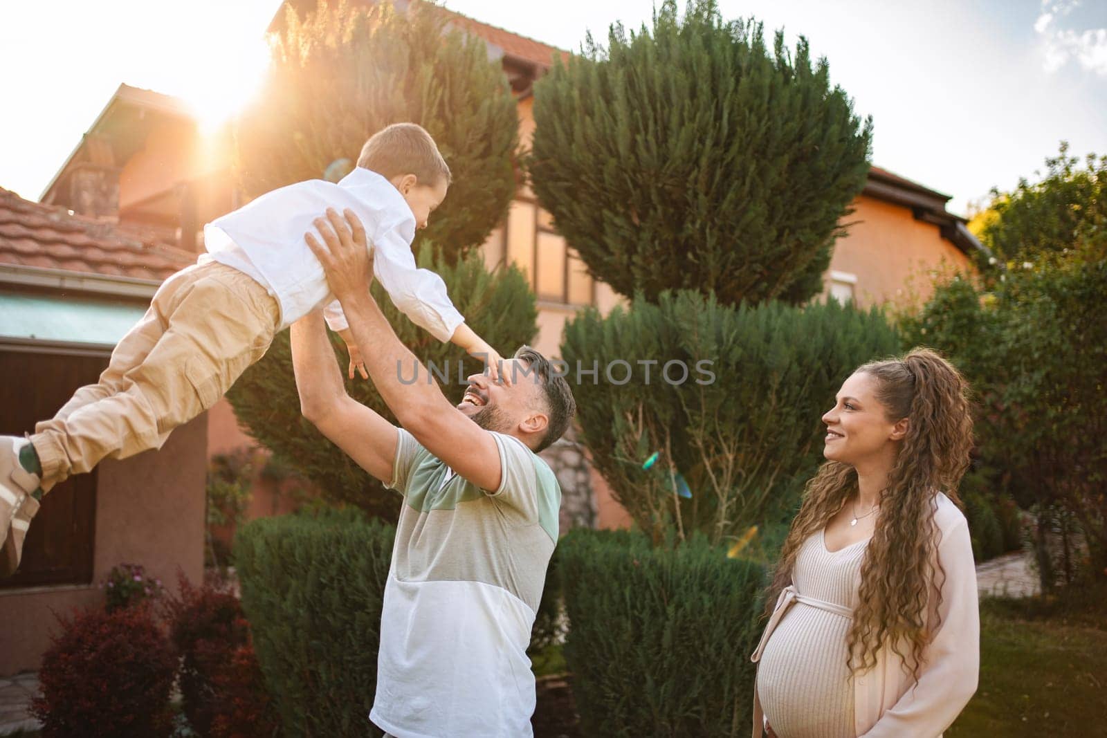 Father lifts son happily while expecting mother smiles nearby