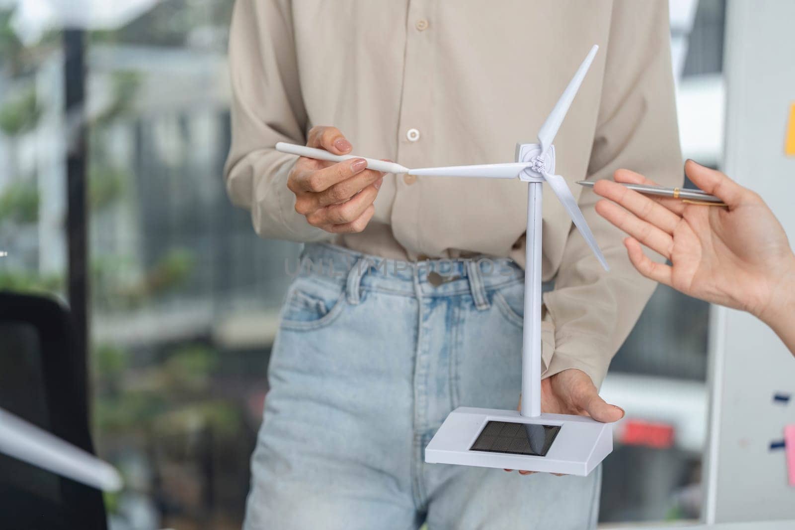 A business professional holds a wind turbine model, discussing sustainable energy solutions and ESG principles in a corporate setting.