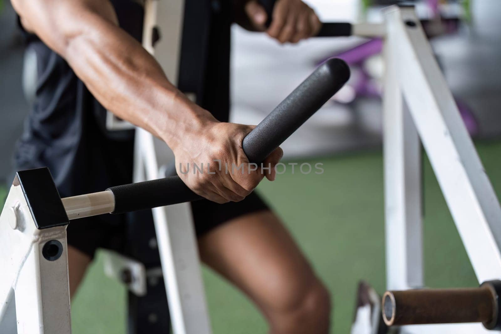 A young man grips gym equipment tightly, emphasizing strength and focus during his fitness training session.