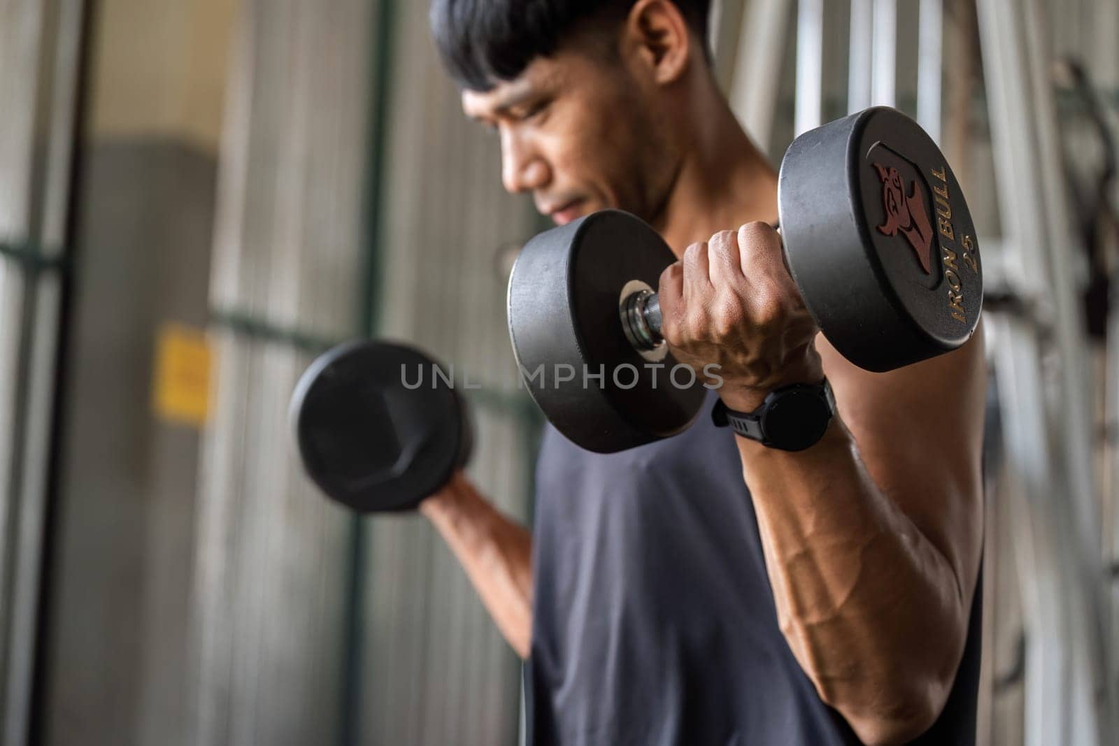 A male fitness enthusiast lifts dumbbells, showcasing muscle definition and commitment to strength training.