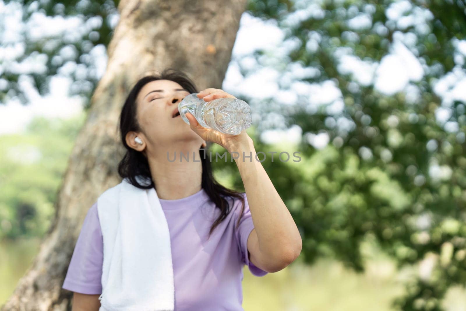 A woman takes a refreshing sip from her water bottle, promoting wellness and hydration after exercising outdoors in nature.