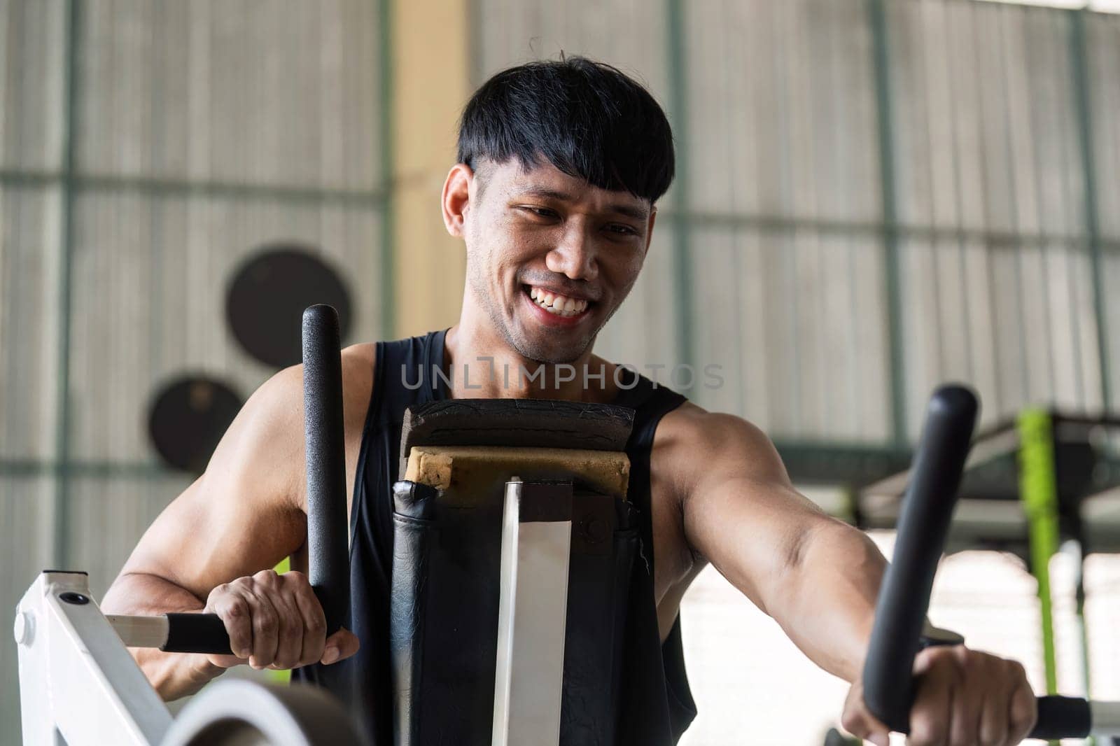 A young man smiles while using gym equipment, showcasing joy and motivation in his fitness journey.