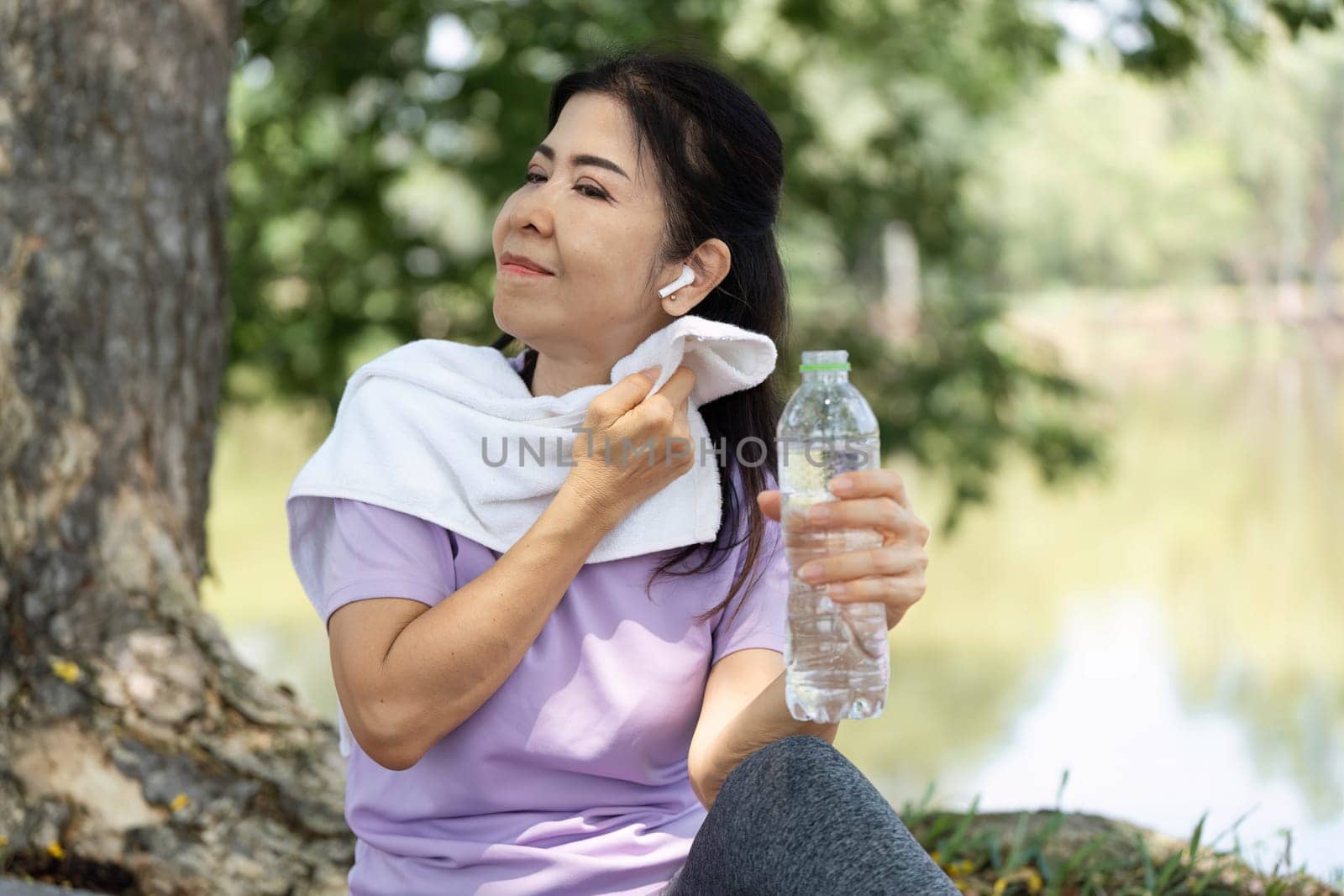 A woman wipes her forehead with a towel, enjoying a refreshing drink of water after an outdoor workout, promoting wellness.
