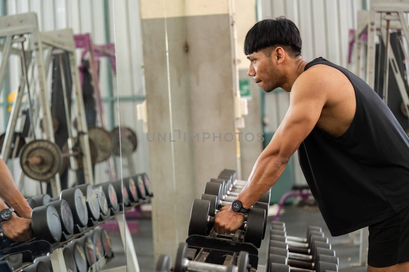 A determined man lifts weights in front of a mirror, focusing on his form and fitness goals at the gym.