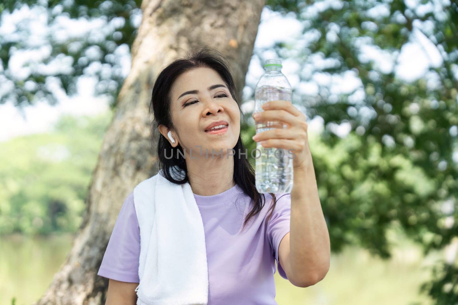 A joyful woman holds a water bottle, enjoying the refreshing taste of hydration after a workout in a peaceful park.