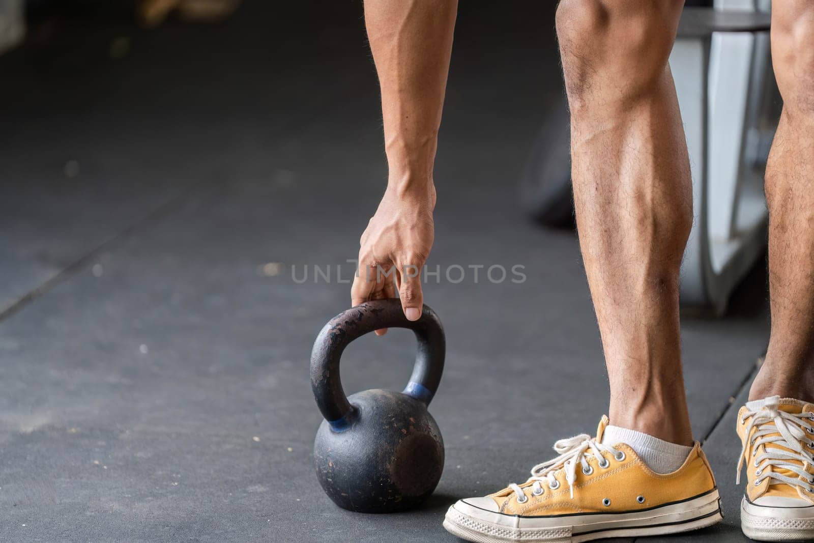 An athlete bends to grasp a kettlebell, emphasizing fitness and strength training in a gym environment.