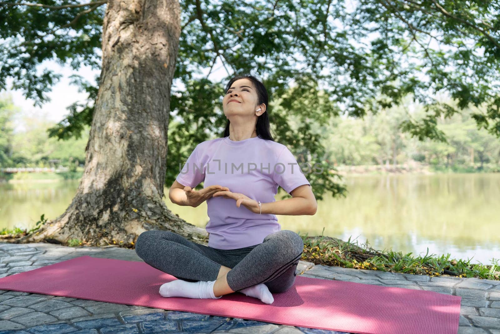A woman sits cross-legged on a yoga mat, practicing mindfulness and meditation in a tranquil lakeside setting.