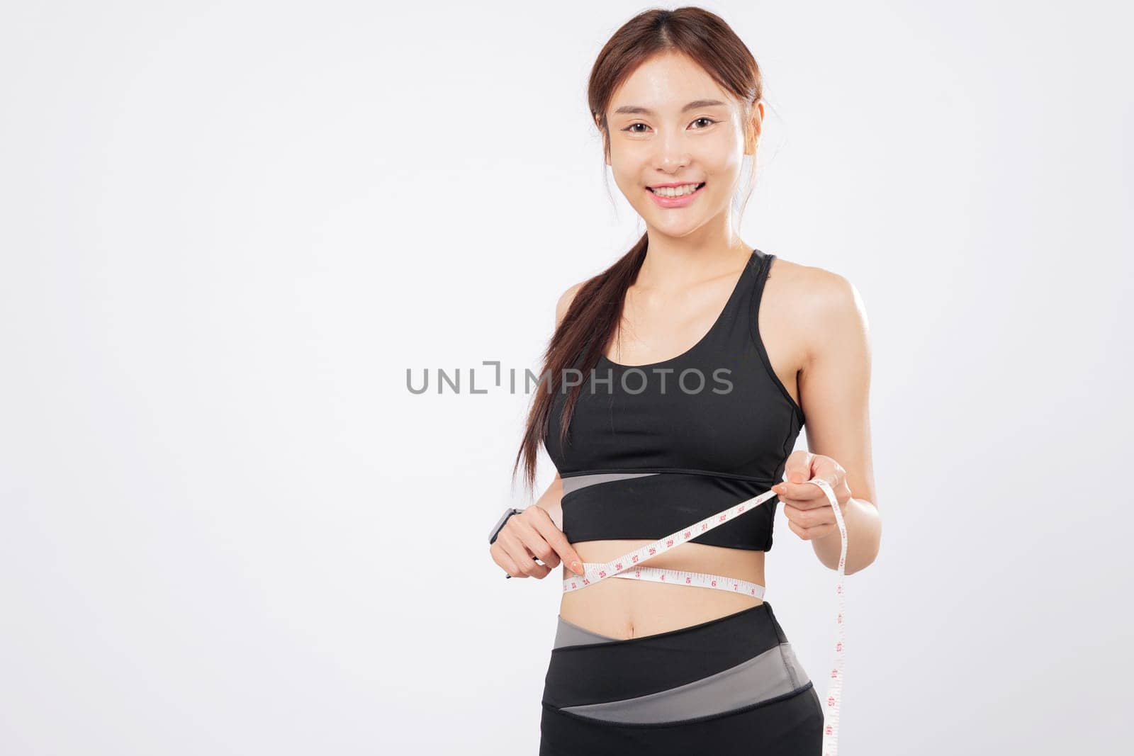 Measure each inch and measure success, this athletic woman in sportswear holds a tape with pride, smiling as she embraces a healthy lifestyle and weight management. isolated studio white background